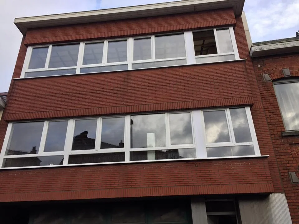 Façade en brique rouge dont les deux niveaux ont été équipés de larges châssis PVC blancs.